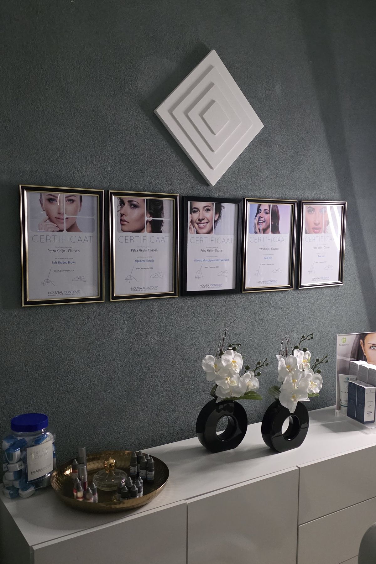 Wand in de salon met witte orchideeën, een wit wandobject en ingelijste certificaten